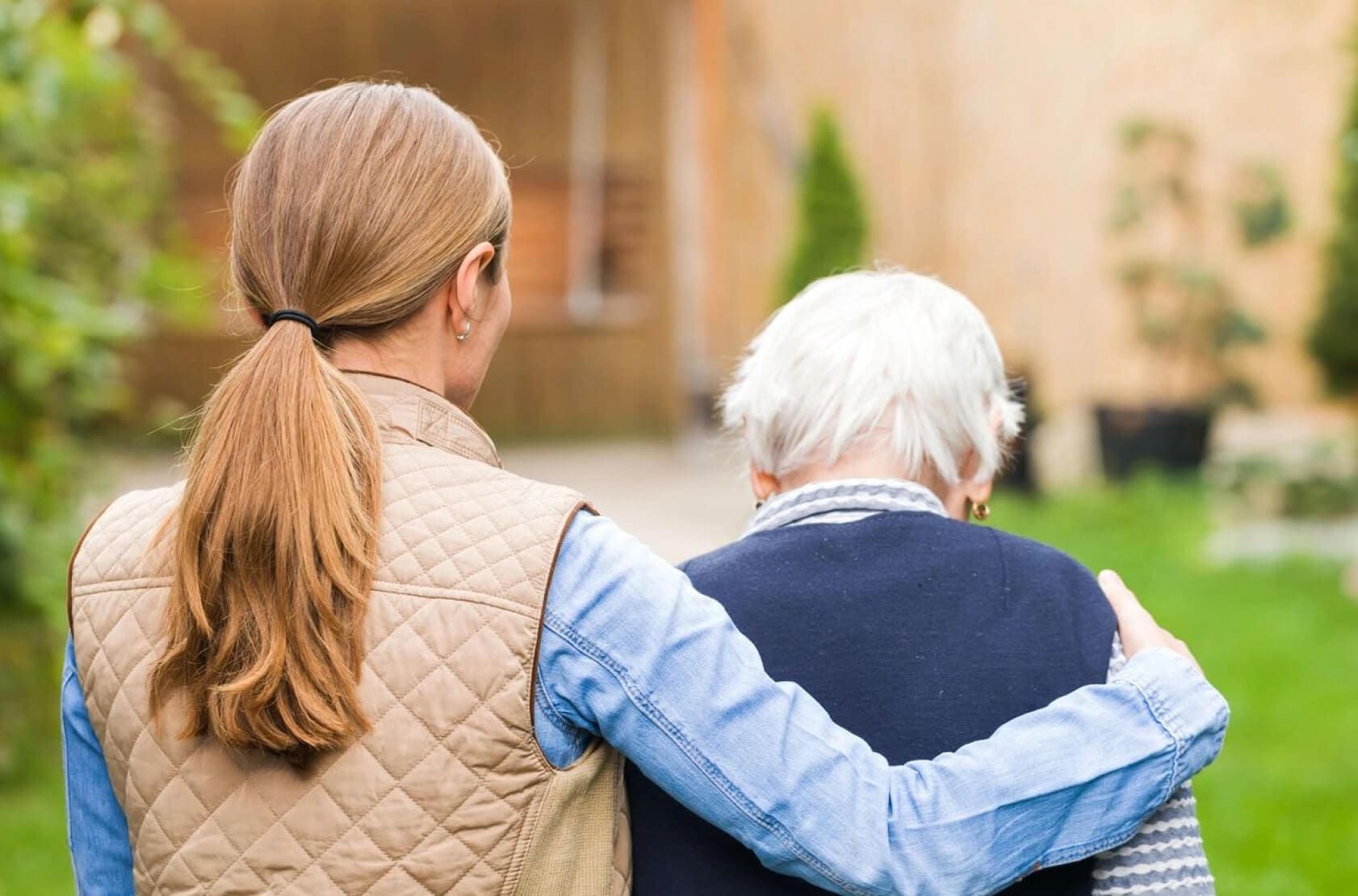 Woman supporting elderly person outdoors.